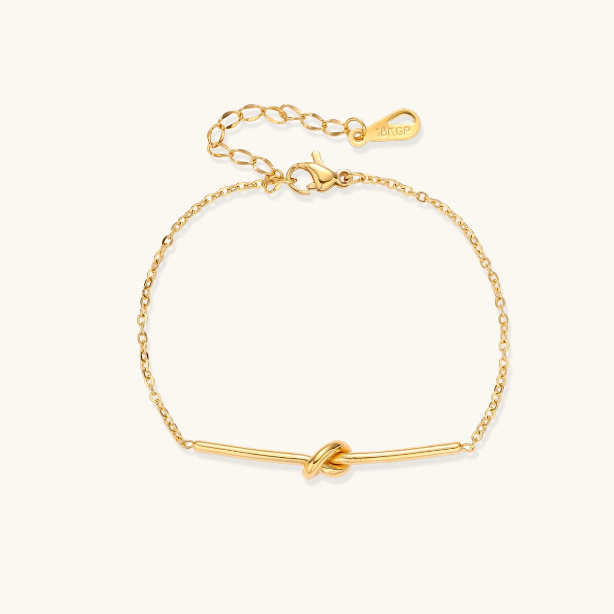 Delicate gold chain bracelet with minimalist bar and centered knot detail on cream background