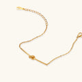 Delicate gold chain bracelet with minimalist bar and centered knot detail on cream background