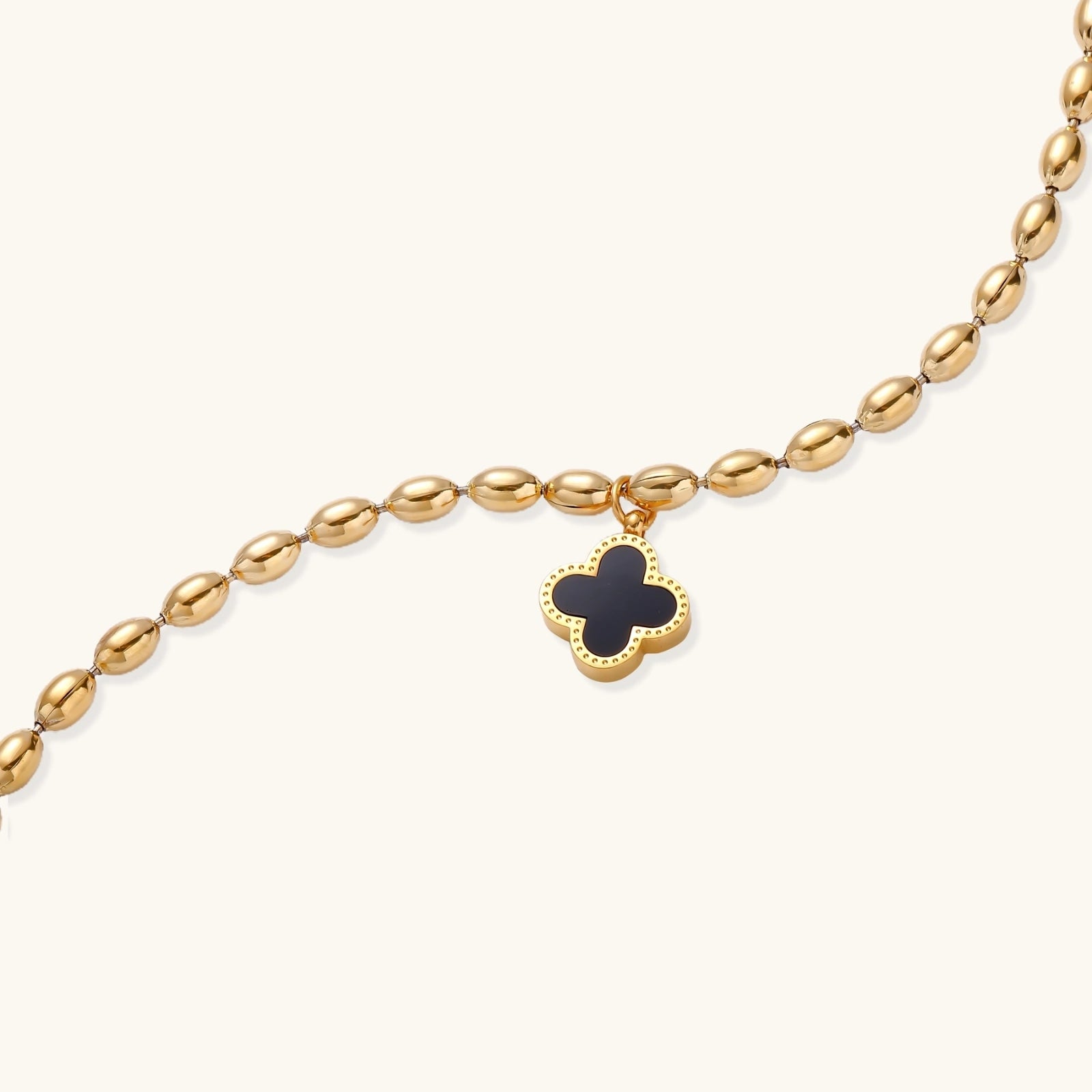 18K gold-plated oval bead bracelet with a four-leaf clover charm in mother-of-pearl or black enamel, adjustable lobster clasp, on white background.