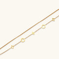 Double-layer gold-plated bracelet with quatrefoil and star charms on cream background, 18K gold finish.