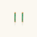 Pair of small gold huggie hoop earrings with bright green cubic zirconia stones on cream background