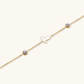 Gold chain bracelet with white mother of pearl butterfly pendant and two bezel-set crystals on cream background