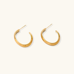 Chunky tubular hoop earrings in warm 14K gold-plated finish with smooth polished surface on cream background.