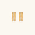 Textured gold huggie hoop earrings with raised ribbed rows creating dimensional sculptural design on cream background