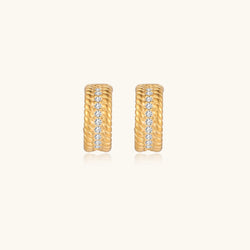 Textured gold huggie hoop earrings with raised ribbed rows creating dimensional sculptural design on cream background