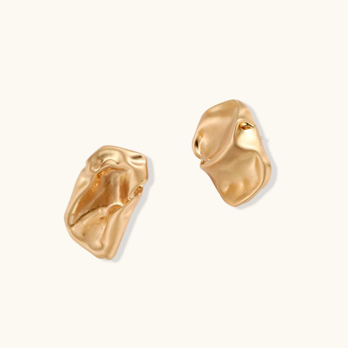 Sculptural gold-toned jewelry set with organic fluid shapes including earrings and layered chain necklace on cream background.