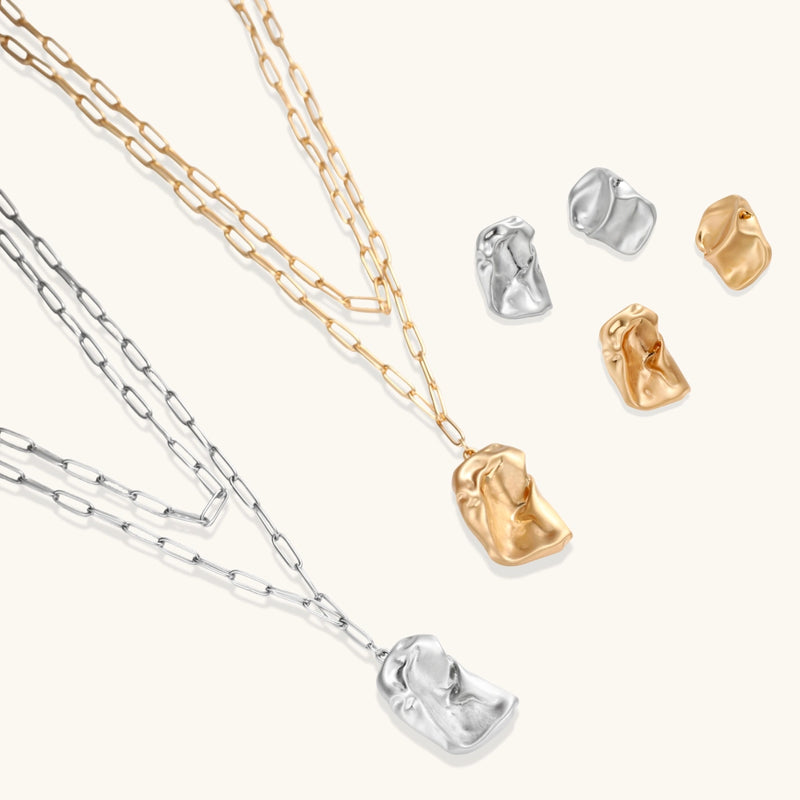 Sculptural gold-toned jewelry set with organic fluid shapes including earrings and layered chain necklace on cream background.