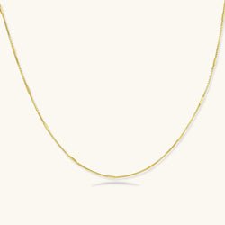 Delicate 14K gold-plated box chain necklace with evenly spaced bar links, shown flat on cream background.