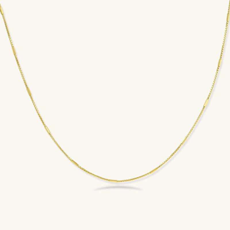 Delicate 14K gold-plated box chain necklace with evenly spaced bar links, shown flat on cream background.