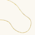 Delicate 14K gold-plated box chain necklace with evenly spaced bar links, shown flat on cream background.