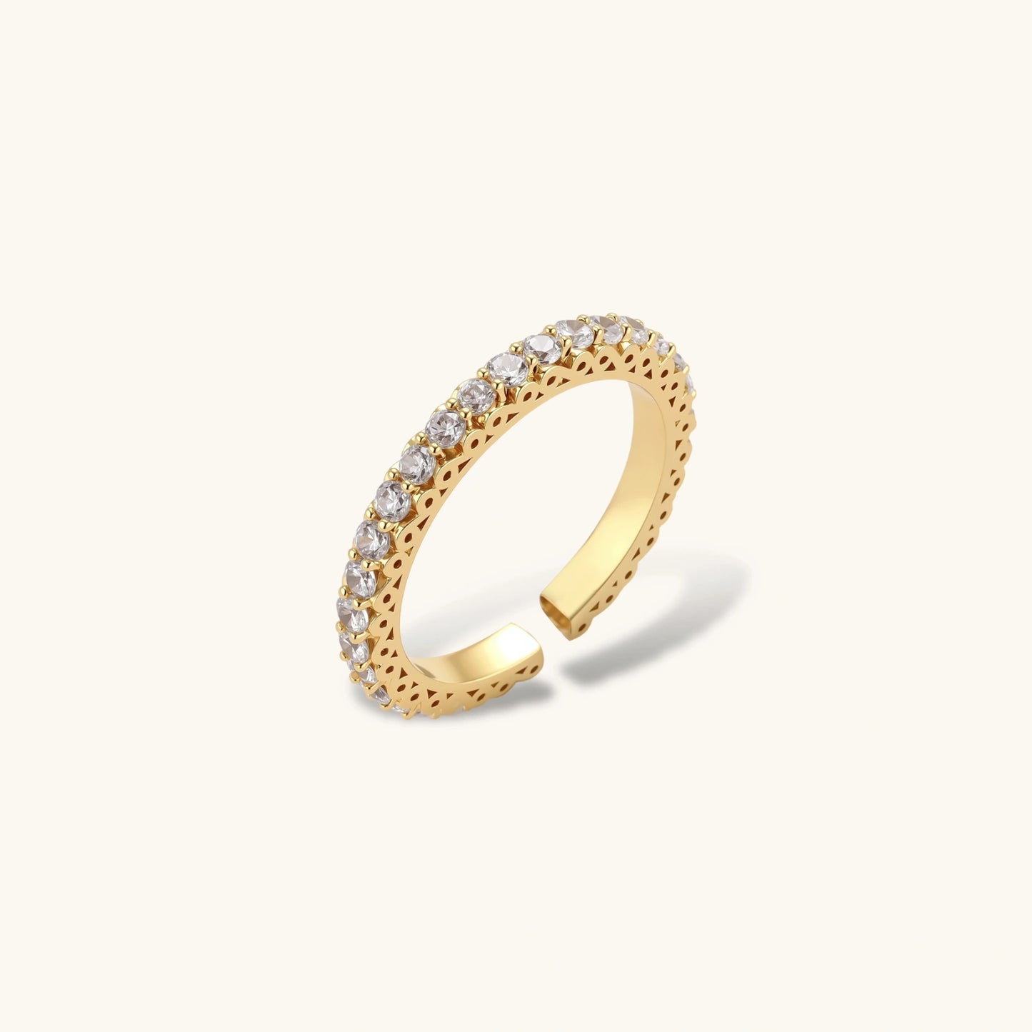 Close-up of adjustable gold-plated ring with continuous row of round zirconia stones on neutral background.