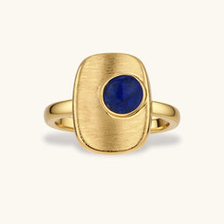 Adjustable gold-plated ring with textured square setting featuring a round blue lapis lazuli stone on cream background.
