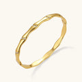Gold-toned wavy bangle with bamboo-style segments and CZ crystal clusters on cream background. 18K plated stainless steel.