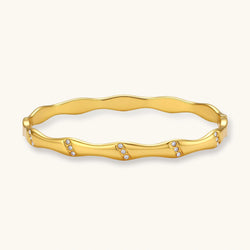 Gold-toned wavy bangle with bamboo-style segments and CZ crystal clusters on cream background. 18K plated stainless steel.