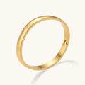 Polished 18K gold plated stainless steel hinge bangle with smooth flat-top profile on cream background.